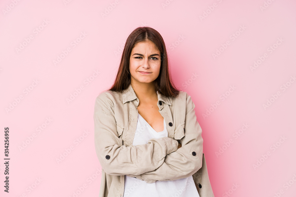 Young caucasian woman posing in a pink background frowning face in displeasure, keeps arms folded. Young caucasian woman posing in a pink background frowning face in displeasure, keeps arms folded.