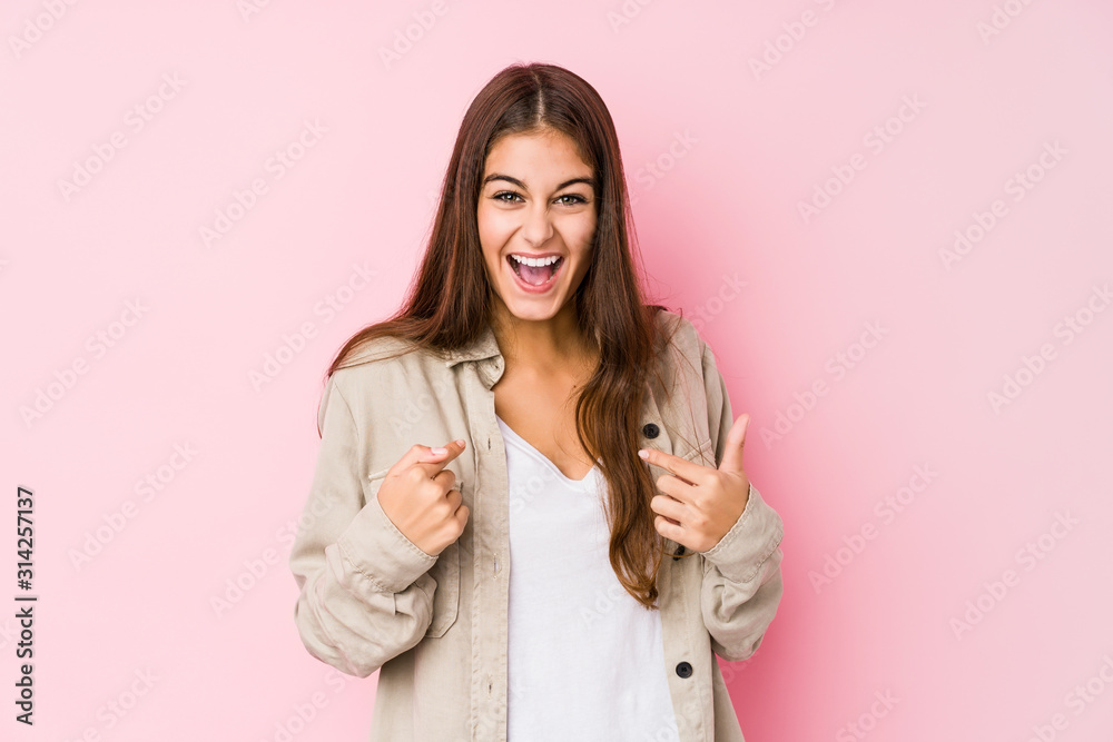 Young caucasian woman posing in a pink background surprised pointing with finger, smiling broadly. Young caucasian woman posing in a pink background surprised pointing with finger, smiling broadly.