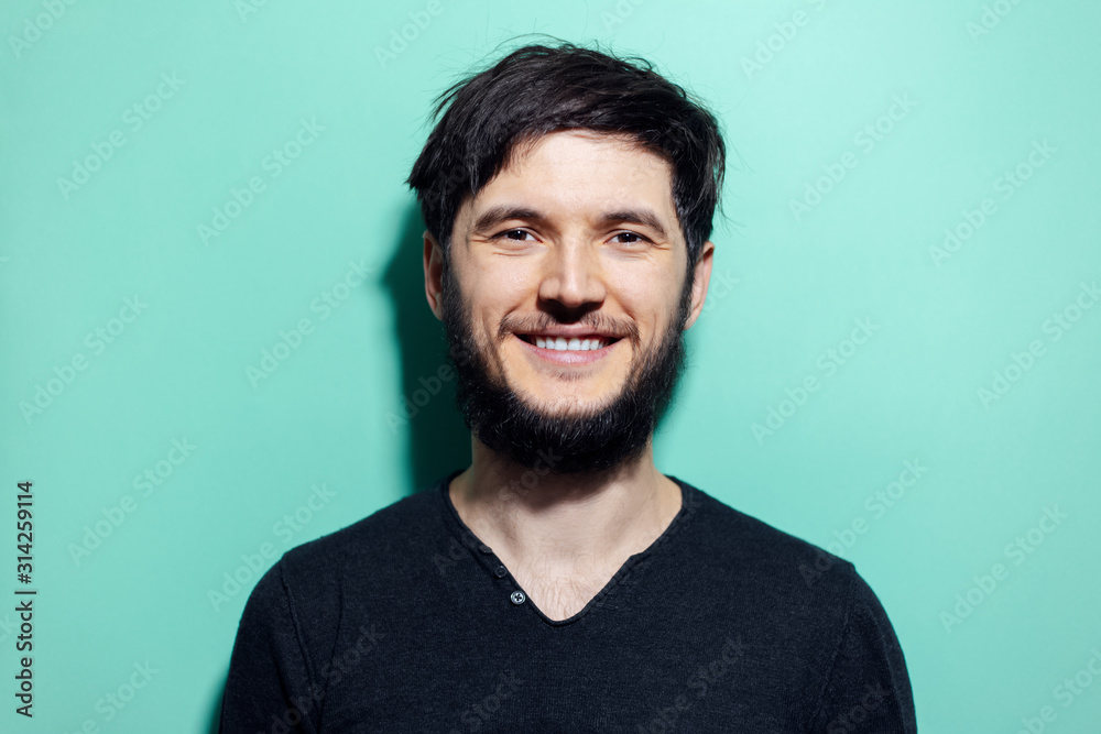 Obraz premium Studio portrait of young smiling bearded man with disheveled hair on background of aqua menthe color.
