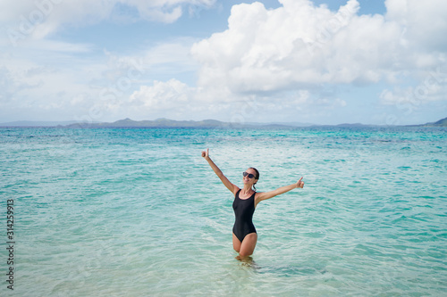 Best vacation! Happy young woman in black swimsuit showing thumb up while swimming on tropical beach. © luengo_ua