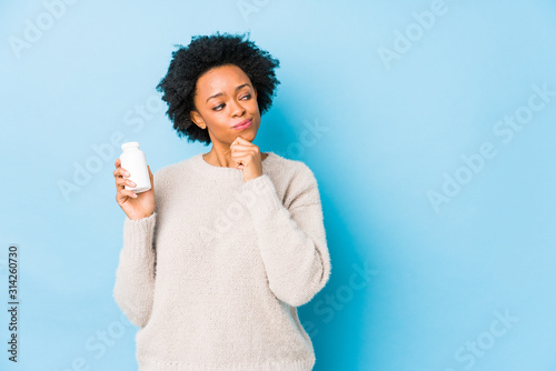 Middle age african american woman holding a vitamin bottle looking sideways with doubtful and skeptical expression. photo