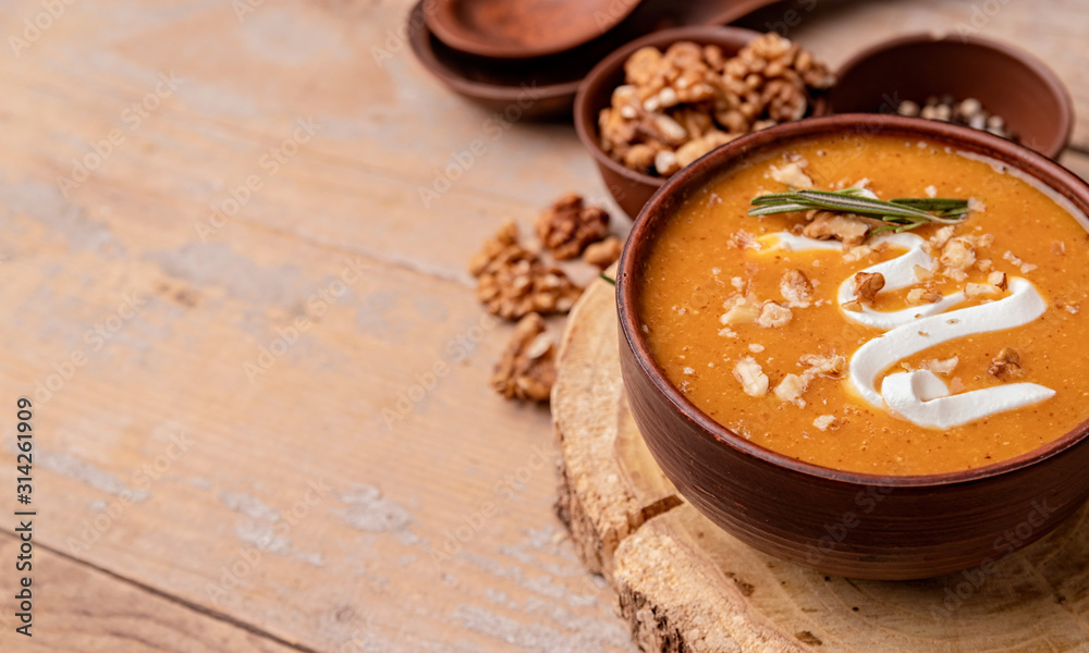 Pumpkin soup with creme in brown bowl decorated with walnuts with copy space on wooden background