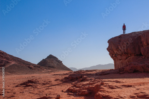 A Caucasian male traveler climbed a rock and stands against the sky in Timna National Park, Israel,