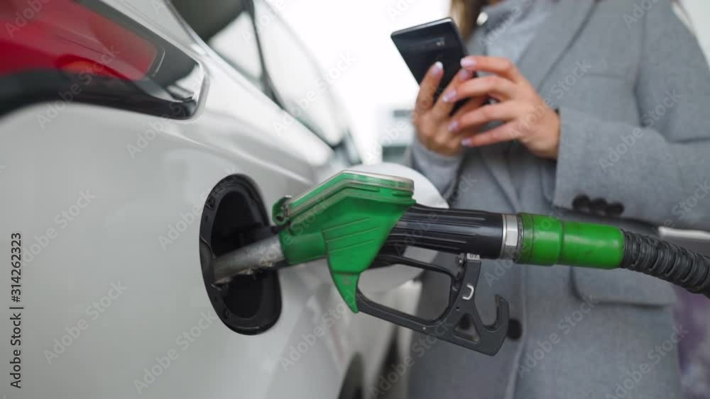 Woman using smartphone while her car is refueling. Slow motion Woman using smartphone while her car is refueling. Slow motion