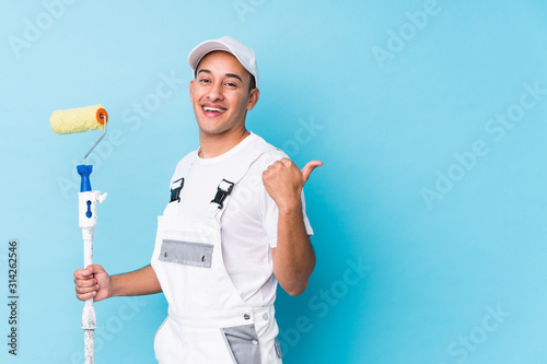 Young professional painter latin man isolated points with thumb finger away, laughing and carefree.