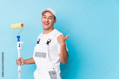 Fototapeta Naklejka Na Ścianę i Meble -  Young professional painter latin man isolated points with thumb finger away, laughing and carefree.
