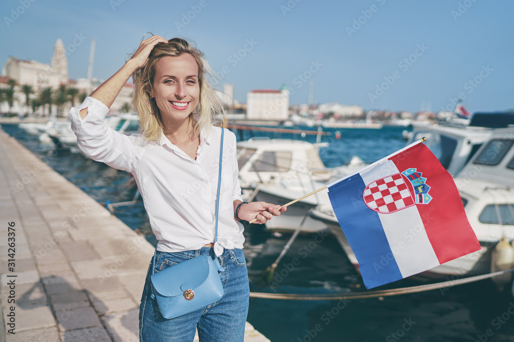 Enjoying vacation in Croatia. Young traveling woman with national croatian flag walking on Split sea shore promenade.