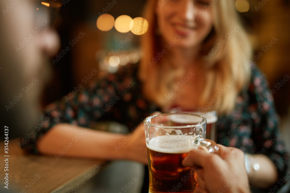 Close up of couple toasting with beer while standing at pub.