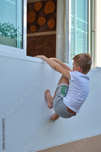 Fototapeta Naklejka Na Ścianę i Meble -  autdoor playIng. A child climbs a wall. Boy climbs into an open window. hide-and-seek on vacation.