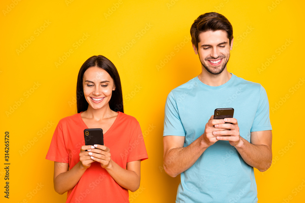 Photo of two funny guy lady people couple hold telephones arms interested reading social network article wear casual blue orange t-shirts isolated yellow color background Photo of two funny guy lady people couple hold telephones arms interested reading social network article wear casual blue orange t-shirts isolated yellow color background