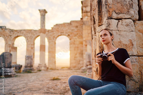 Tourism and hobby. Happy young woman taking photo of ancient antique city Volubilis. Traveling by Morocco.
