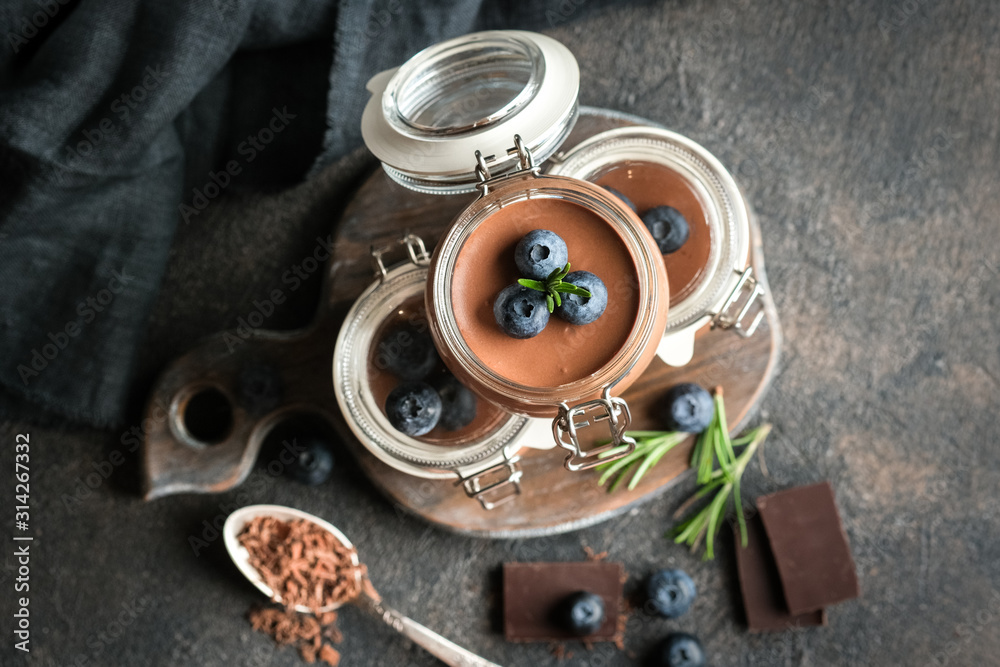 Fototapeta premium Chocolate mousse in glass jar with berries on a dark background copy space. Homemade dessert. Top view.