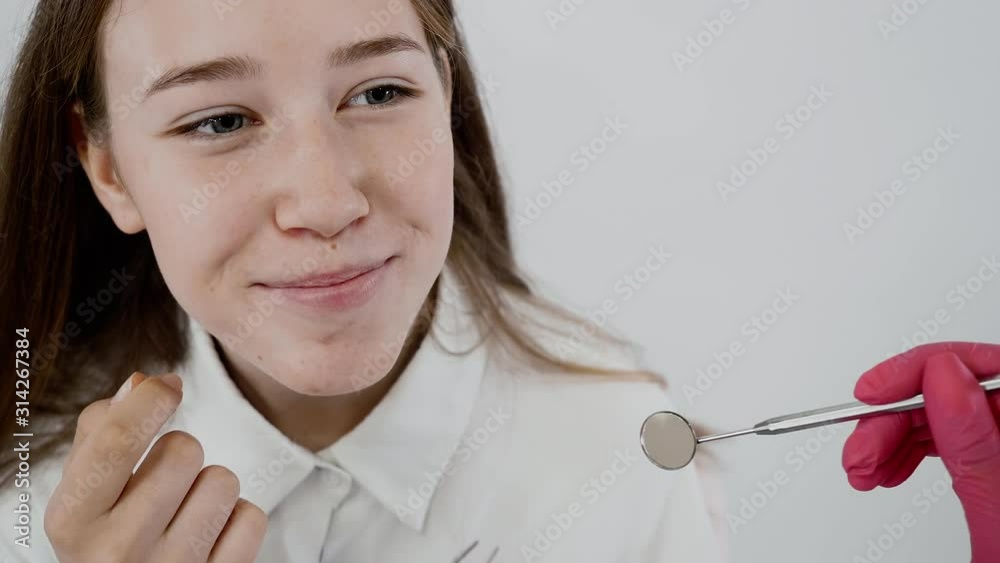 Girl closeup isolated on white background. Examination of oral cavity of patient by dentist using sterilie equipment. Gloved hand check dental condition with mirror. Dental care and healthcare concept Girl closeup isolated on white background. Examination of oral cavity of patient by dentist using sterilie equipment. Gloved hand check dental condition with mirror. Dental care and healthcare concept