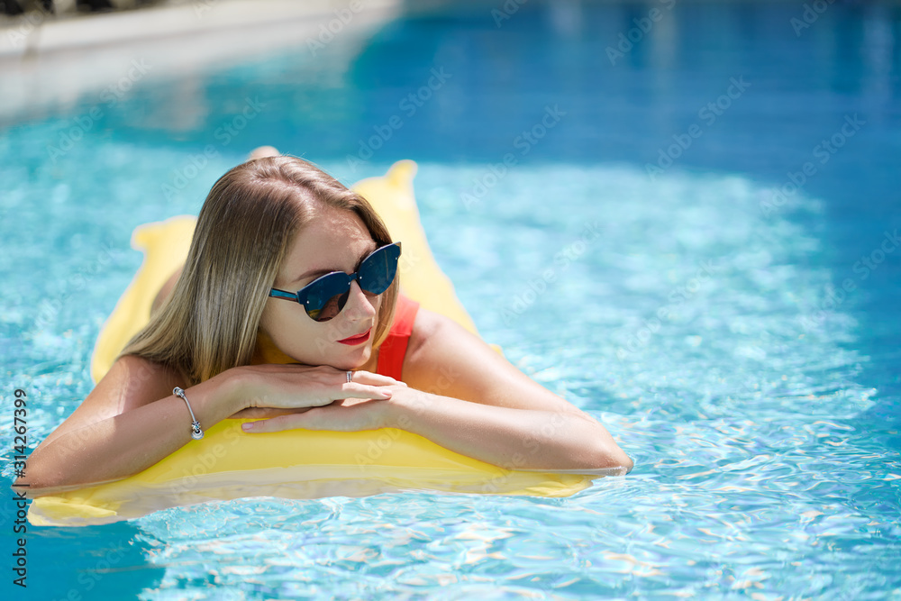 Enjoying suntan. Vacation concept. Slim young woman in bikini on the yellow air mattress in the swimming pool.