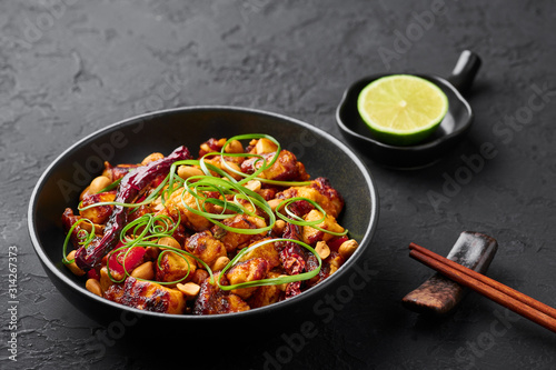 Kung Pao Paneer at black slate background. Kung Pao Paneer is a vegetarian version of chinese sichuan dish Gong Bao with paneer cheese, peanuts, chilli peppers, sauces and onion.