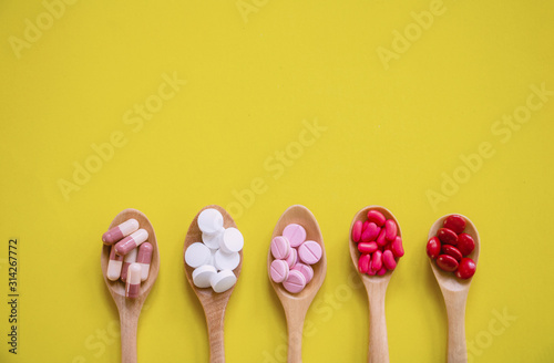 Top view Medicine on wood spoon.Assorted pharmaceutical red capsules with Multi color vitamins and supplements.They are on Yellow background and copy space.Photo concept healthy and medication.