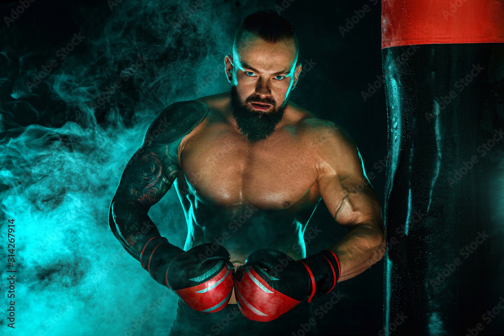 Boxer fighting in gloves with boxing punching bag. Sportsman with tattoos, man Isolated on black background with smoke. Copy Space.