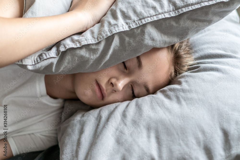Woman with insomnia lying in bed with her head under her pillow trying to sleep. Insomnia and sleep problems. Relax and sleep concept. Feels sleepy and tired.
