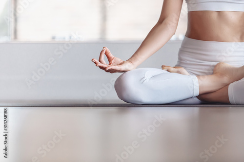 Young beautiful girl meditates in lotus pose sitting by the large windows of country house. Concept of relaxation and meditation. Ardha Padmasana exercise, meditating in Lotus pose with mudra gesture