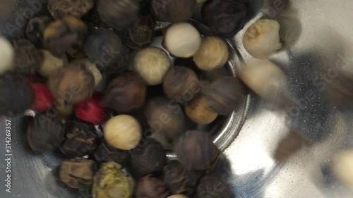 Dry mix peppercorns fall in a metal funnel. High angle view. photo