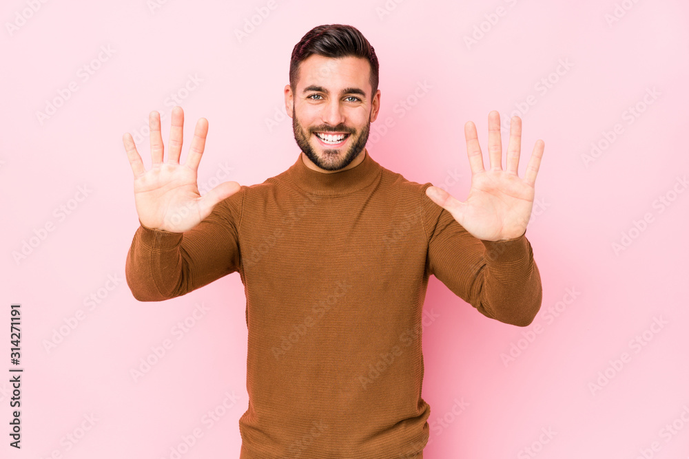 Young caucasian man against a pink background isolated showing number ten with hands.