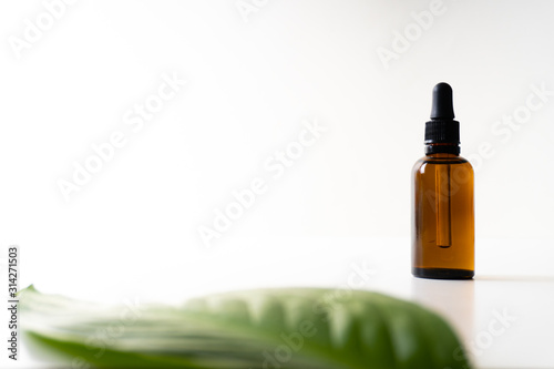 A small bottle with a dropper full of CBD oil or any other oil and a green leaf on white background