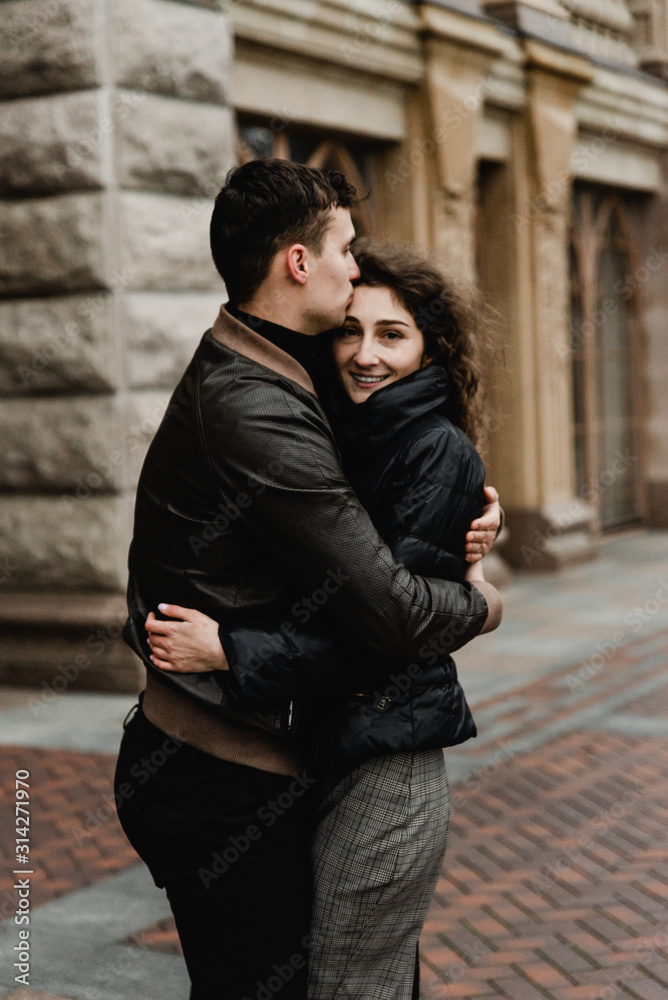 Attractive young couple walking near castle. Wife and husband kissing and holding hands on background of ancient building. Two smiling lovers. Family and love concept