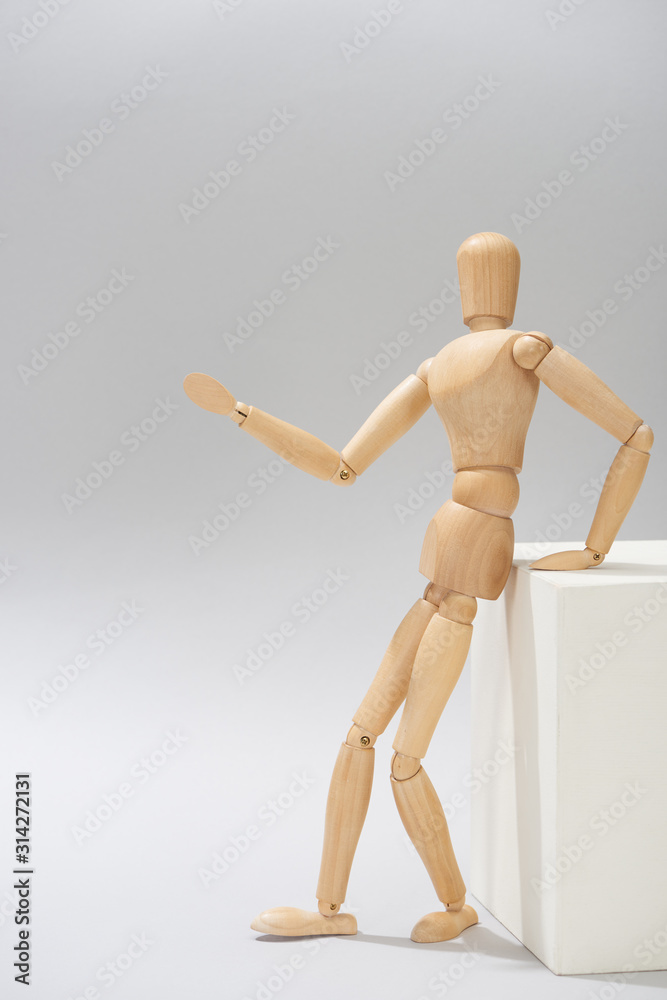 Wooden dummy by white stand pointing with hand on grey background Wooden dummy by white stand pointing with hand on grey background