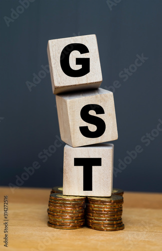 GST. Good and Services Tax on wooden block on stacked coins