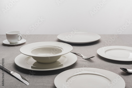 Empty tableware with coffee cup on tablecloth on gey background