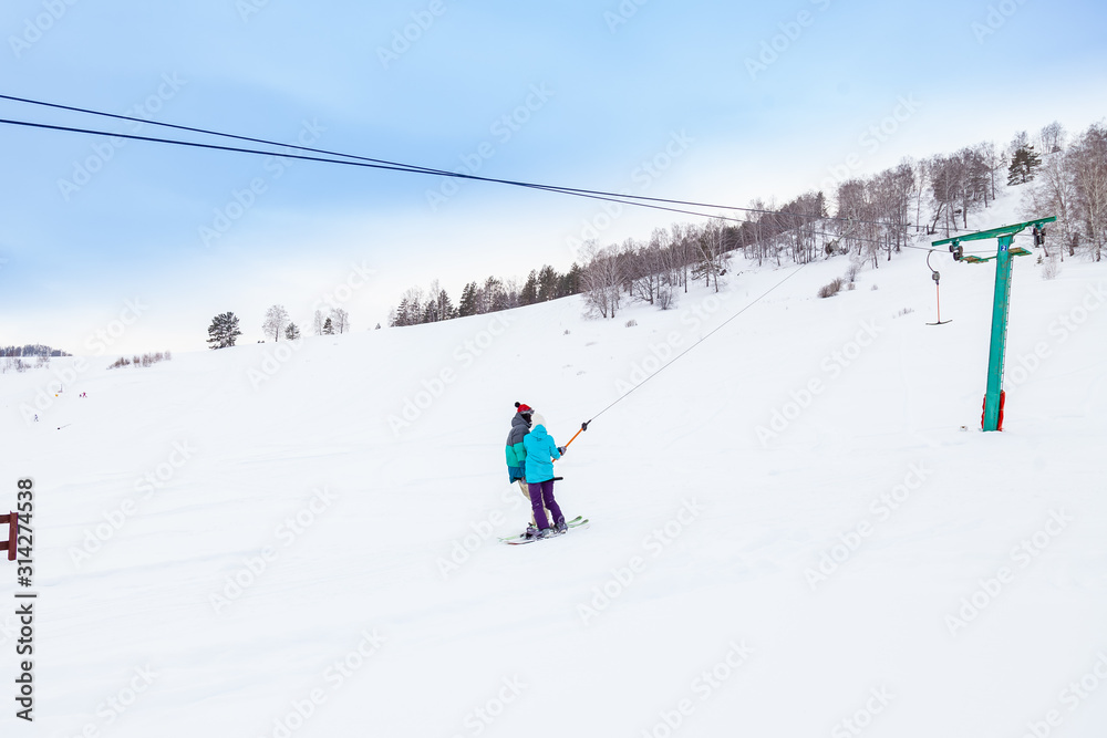 A man skier climbs a mountain through the white snow clinging to a rope of a tow rope in a sports tourist base Turquoise Katun. Seasonal sports.