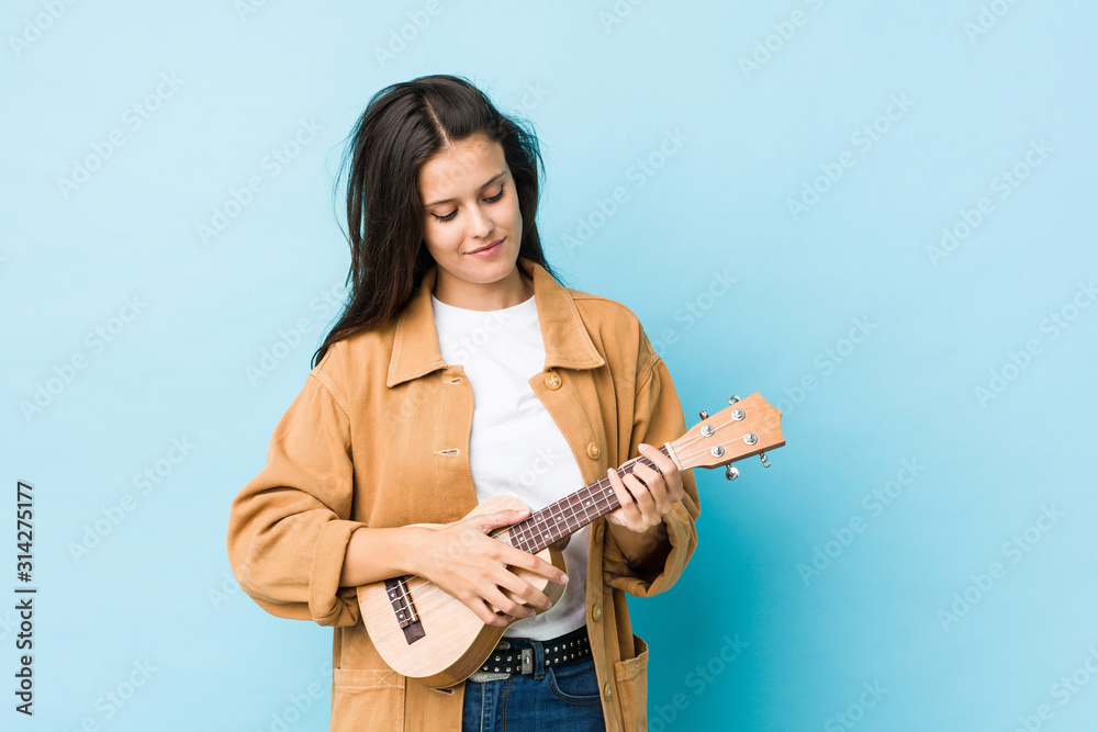 Young caucasian woman playing ukelele isolated on a blue background Young caucasian woman playing ukelele isolated on a blue background