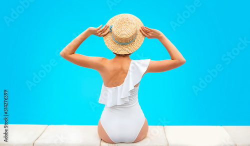 beautiful redhead (ginger) woman's back in the white swimminig suit sitting by the swimming pool (or sea or ocean) in the straw hat in summer day. Summer, relax, wellness, recreation concept photo