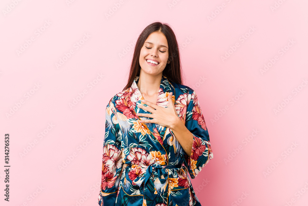 Young caucasian woman wearing a kimono pajama laughs out loudly keeping hand on chest. Young caucasian woman wearing a kimono pajama laughs out loudly keeping hand on chest.