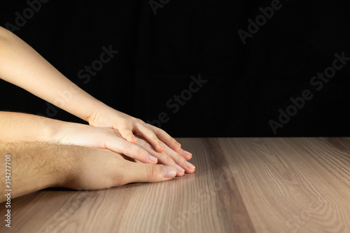 Family hands clasped together. The palms of dad, mom and son. Concept for charitable community and family support. Close-up of male, female and child arms on table with wooden texture.
