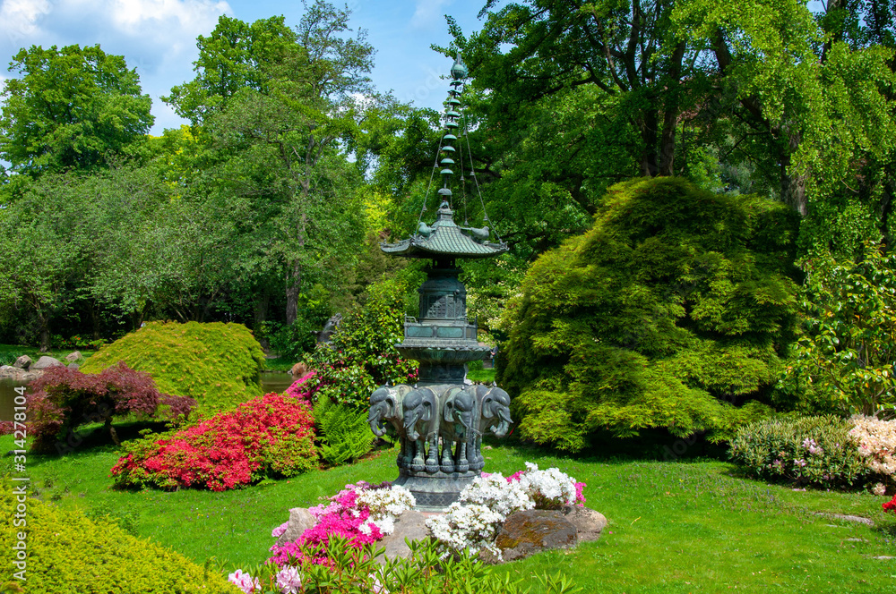 An asian-styled fountain statue surrounded by flowers in a park An asian-styled fountain statue surrounded by flowers in a park