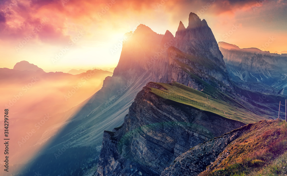 Colorful evening Scene at Gardena valley during sunset. Bright sky over the Seceda peak glowing Sunlight. Amazing Nature Landscape. Sass Rigais and Furchetta mountains. Geisler Group. Dolomites Alps