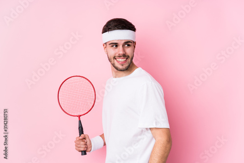 Young caucasian man playing badminton isolated looks aside smiling, cheerful and pleasant. © Asier