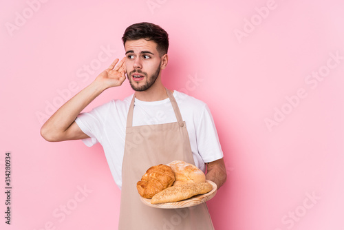 Fototapeta Young caucasian baker man isolated trying to listening a gossip.