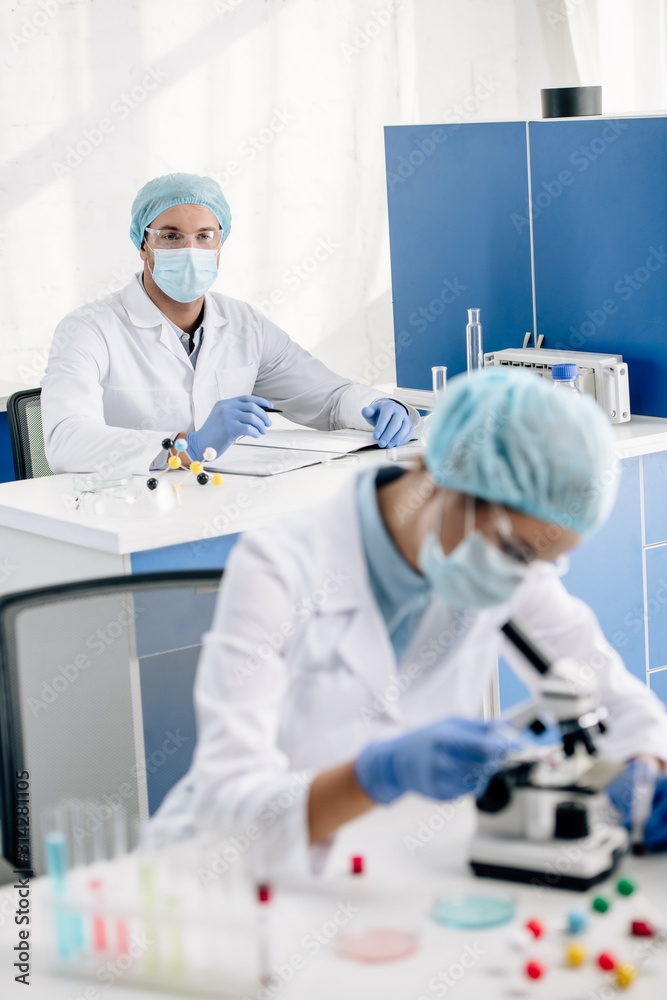 selective focus of genetic consultant looking at colleague with microscope selective focus of genetic consultant looking at colleague with microscope