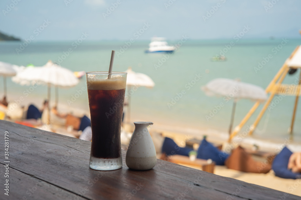 Cold black coffee and syrup over terrace wood with beach and sea background Cold black coffee and syrup over terrace wood with beach and sea background