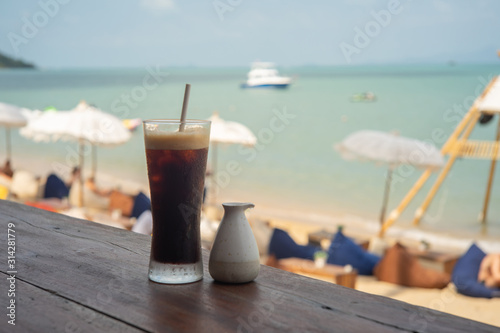 Cold black coffee and syrup over terrace wood with beach and sea background