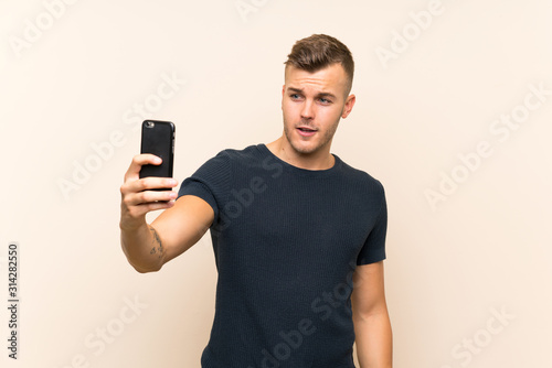 Young handsome blonde man over isolated background making a selfie © luismolinero
