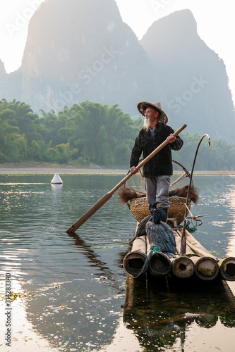 Photography A fisherman and his cormorants on a raft in sunset
