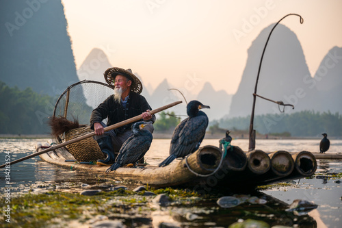 Photography A fisherman and his cormorants on a raft in sunset