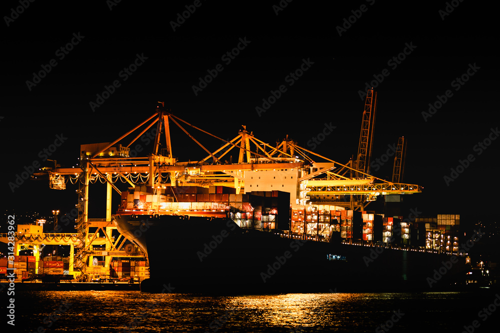 Night view of trieste harbor from the mediterranean sea. disembarkation of a container ship with yellow cranes.