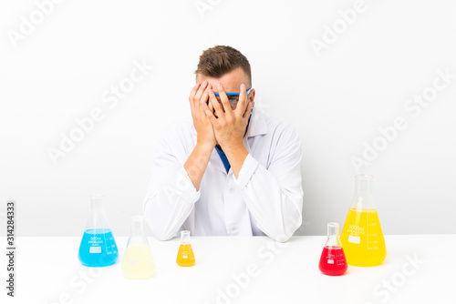 Young scientific with lots of laboratory flask covering eyes and looking through fingers