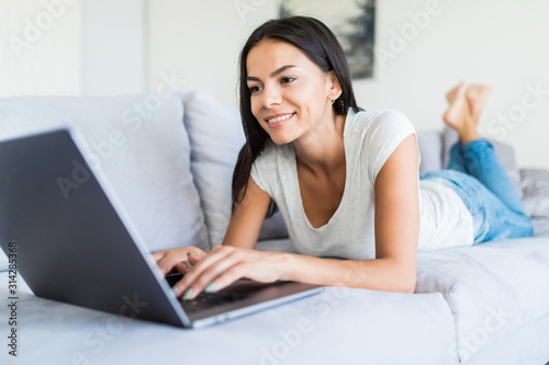 Young smiling woman lying down the bed in front of her laptop with her legs raised slightly
