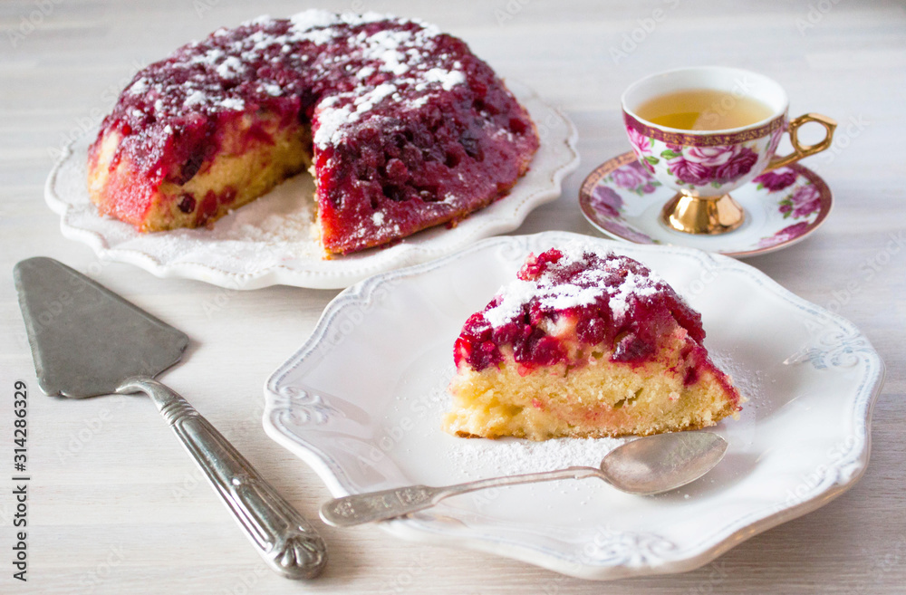 Piece of cranberry tart, pie, cake on plate, tea spoon, cup of tea on white wooden table backgound Piece of cranberry tart, pie, cake on plate, tea spoon, cup of tea on white wooden table backgound