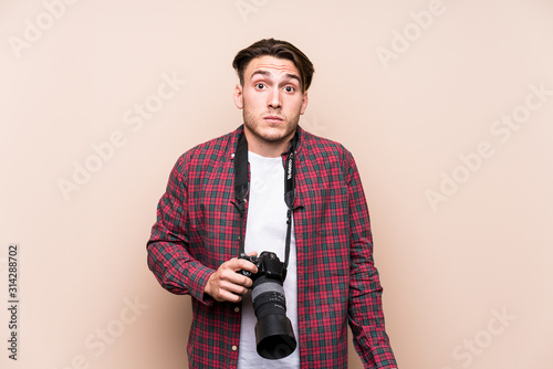 Young caucasian photographer man isolated shrugs shoulders and open eyes confused.
